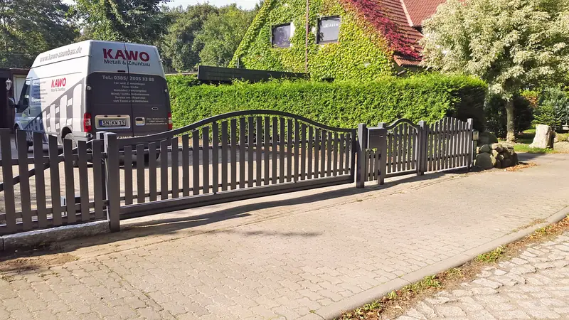 Anthrazitfarbener Aluminiumzaun mit geschwungener Oberkante entlang eines Gehwegs